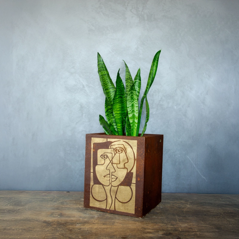 Kwadratowa osłonka loft w efekcie kortenu z ręcznie malowaną, złotą geometryczną twarzą.