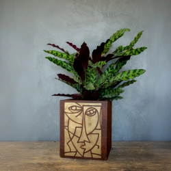 Kwadratowa osłonka loft z efektem kortenu i ręcznie malowaną złotą geometryczną twarzą.