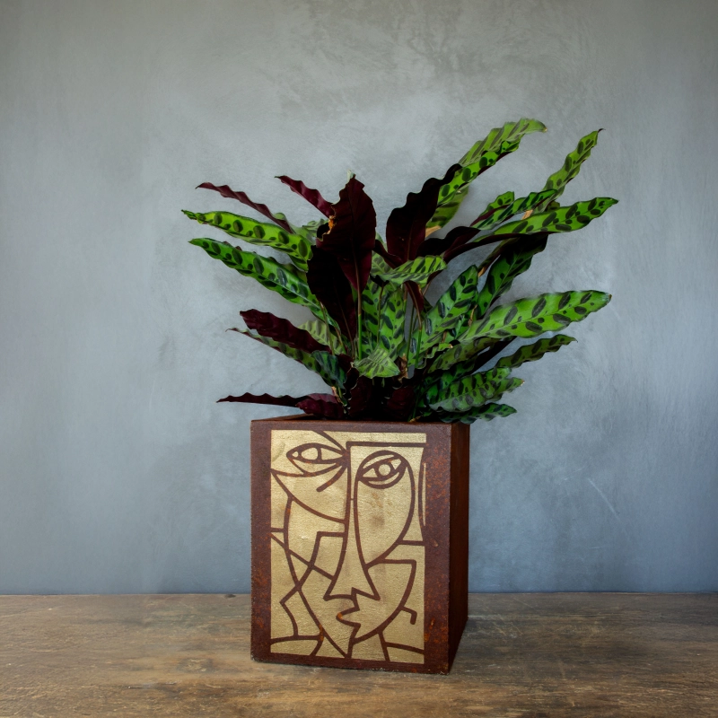 Kwadratowa osłonka loft z efektem kortenu i ręcznie malowaną złotą geometryczną twarzą.