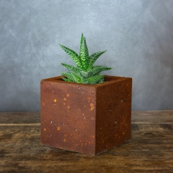 Kwadratowa betonowa osłonka z rdzawym efektem kortenu, wykonana z betonu portlandzkiego.