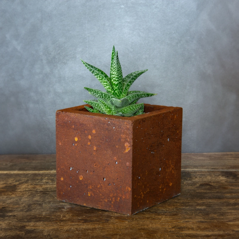 Kwadratowa betonowa osłonka z rdzawym efektem kortenu, wykonana z betonu portlandzkiego.