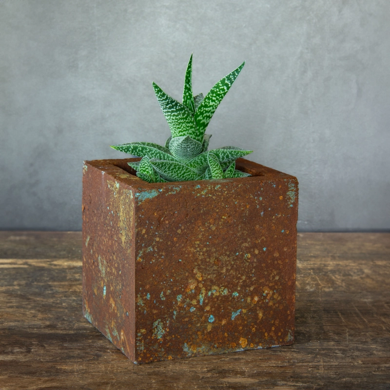 Kwadratowa osłonka z betonu portlandzkiego z intensywnym efektem rdzy i turkusowej patyny.